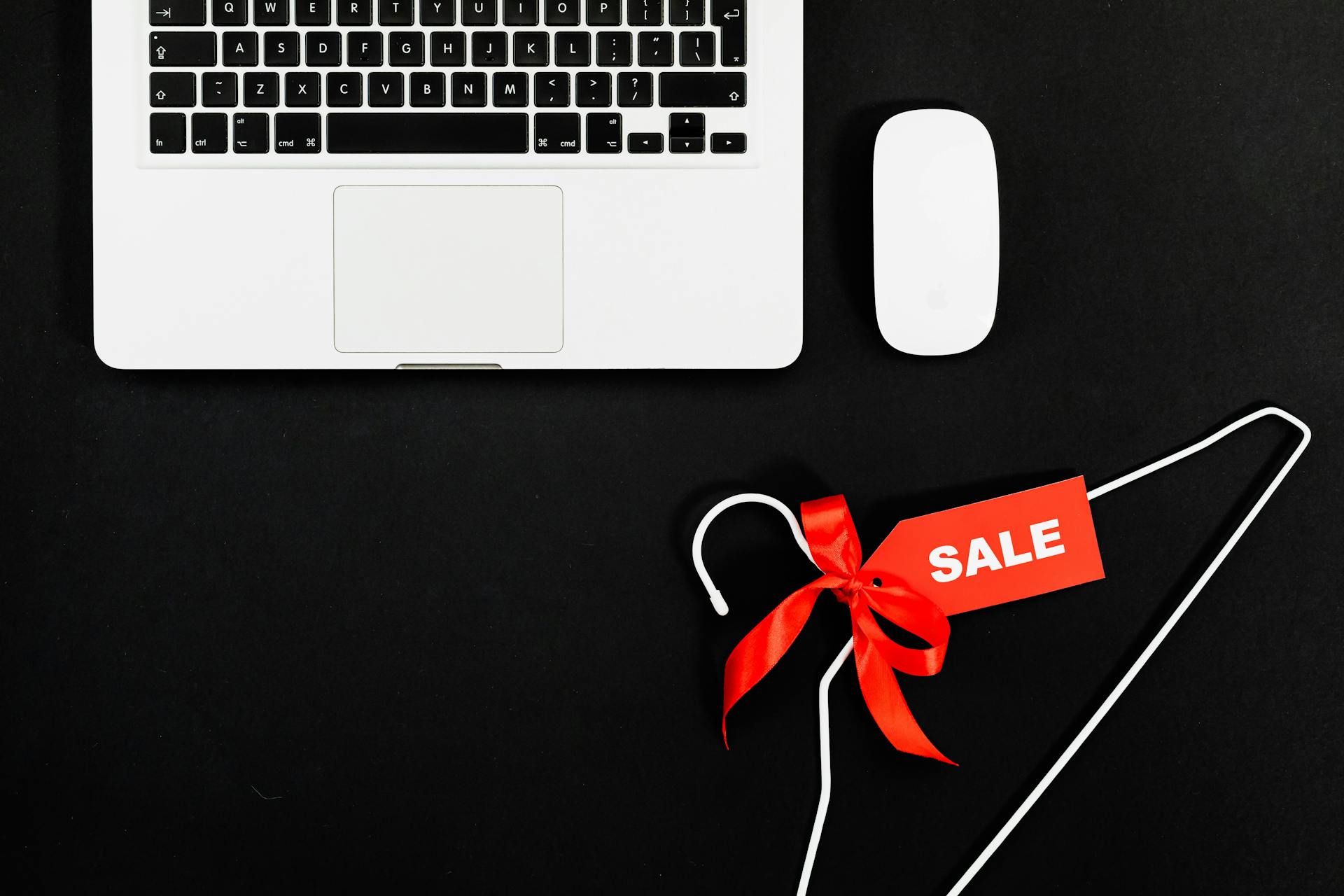 White laptop and mouse on a black background with a red sale tag tied to a hanger, symbolizing online holiday promotions and the need for speed optimization for Shopify during peak shopping events.