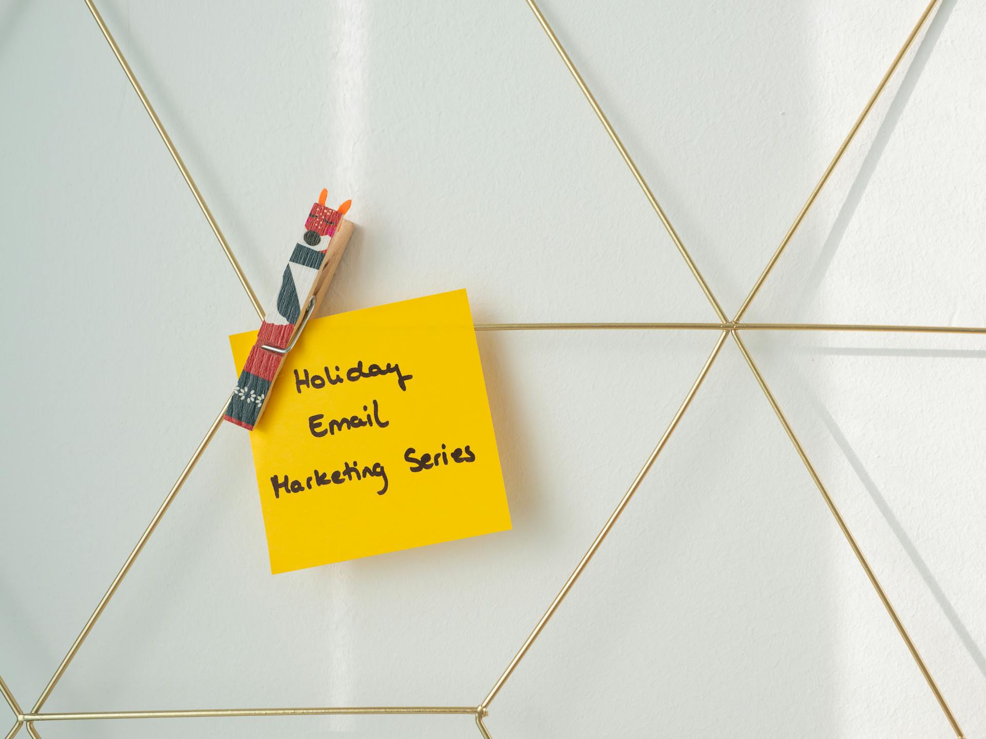 Yellow sticky note clipped to a wire grid with “Holiday Email Marketing Series” handwritten on it, representing seasonal ecommerce email marketing planning.