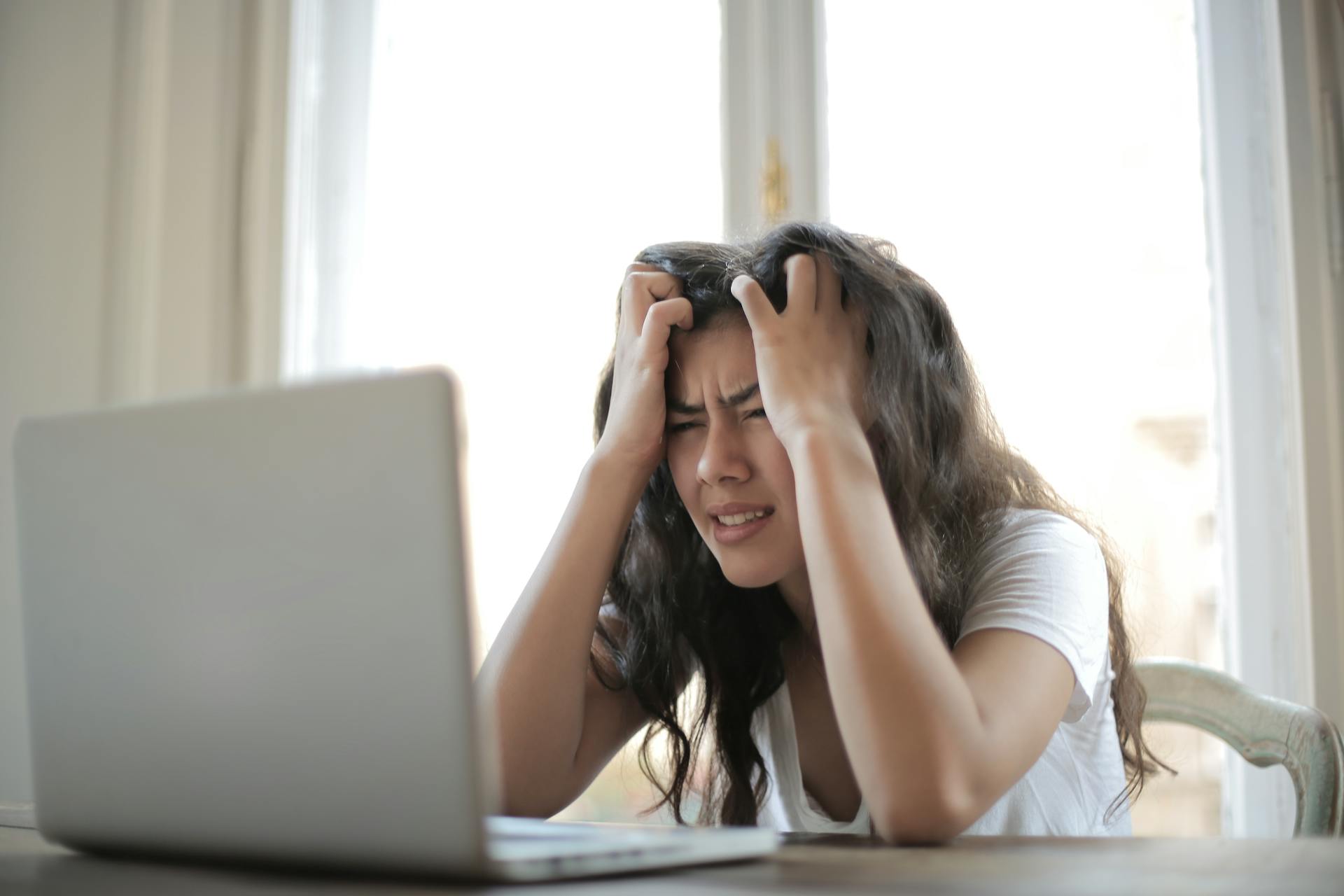 Frustrated woman pulling her hair while using a laptop, representing poor user experience, slow ecommerce websites, and customer retention challenges.