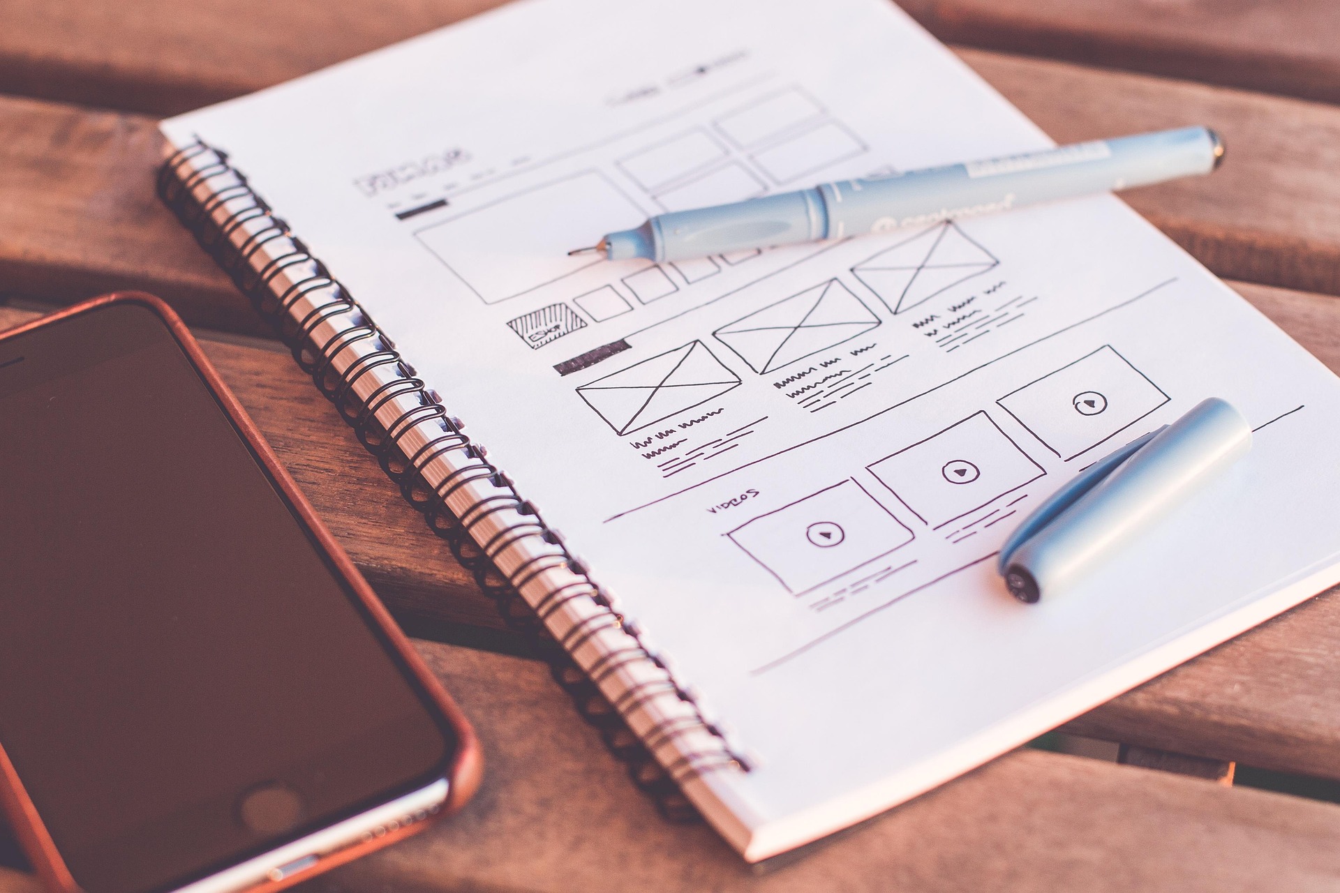 Website wireframe sketch on notebook beside smartphone, representing design planning to improve average session duration