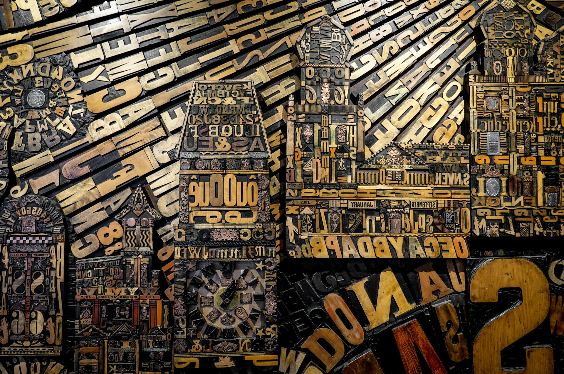 Artistic collage of vintage woodblock letters and numbers arranged into buildings and abstract shapes, showcasing the historical roots of typography and influence on modern web fonts.