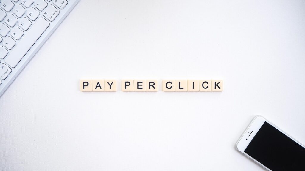 Scrabble tiles spelling out ‘Pay Per Click’ on a white background, with a smartphone and keyboard nearby — representing paid ads, PPC advertising, and digital marketing strategy.