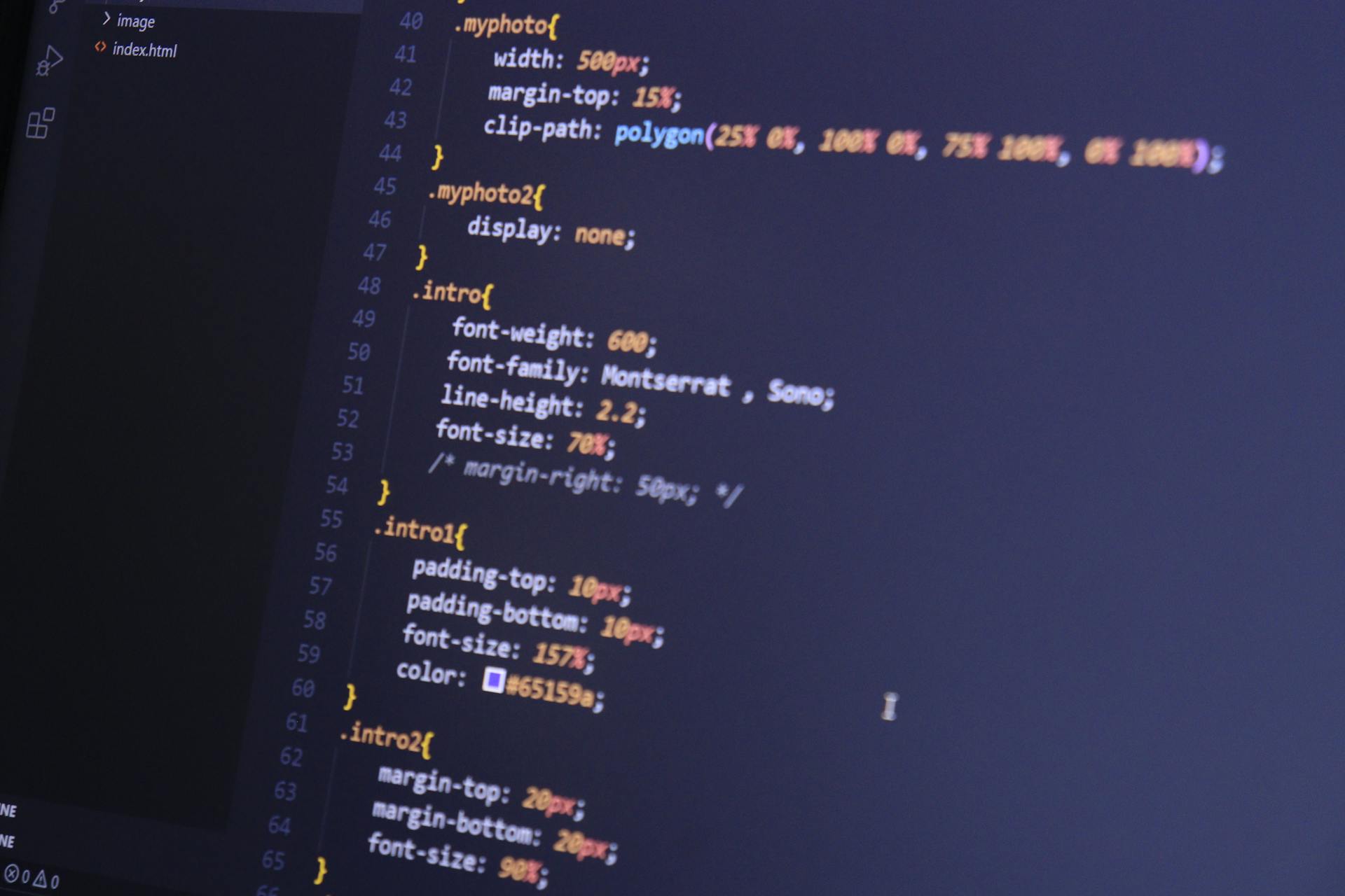 Close-up of CSS code in a developer editor showing web fonts configuration, including font-family, font-weight, and responsive styling for HTML elements using Montserrat and Sono typefaces.