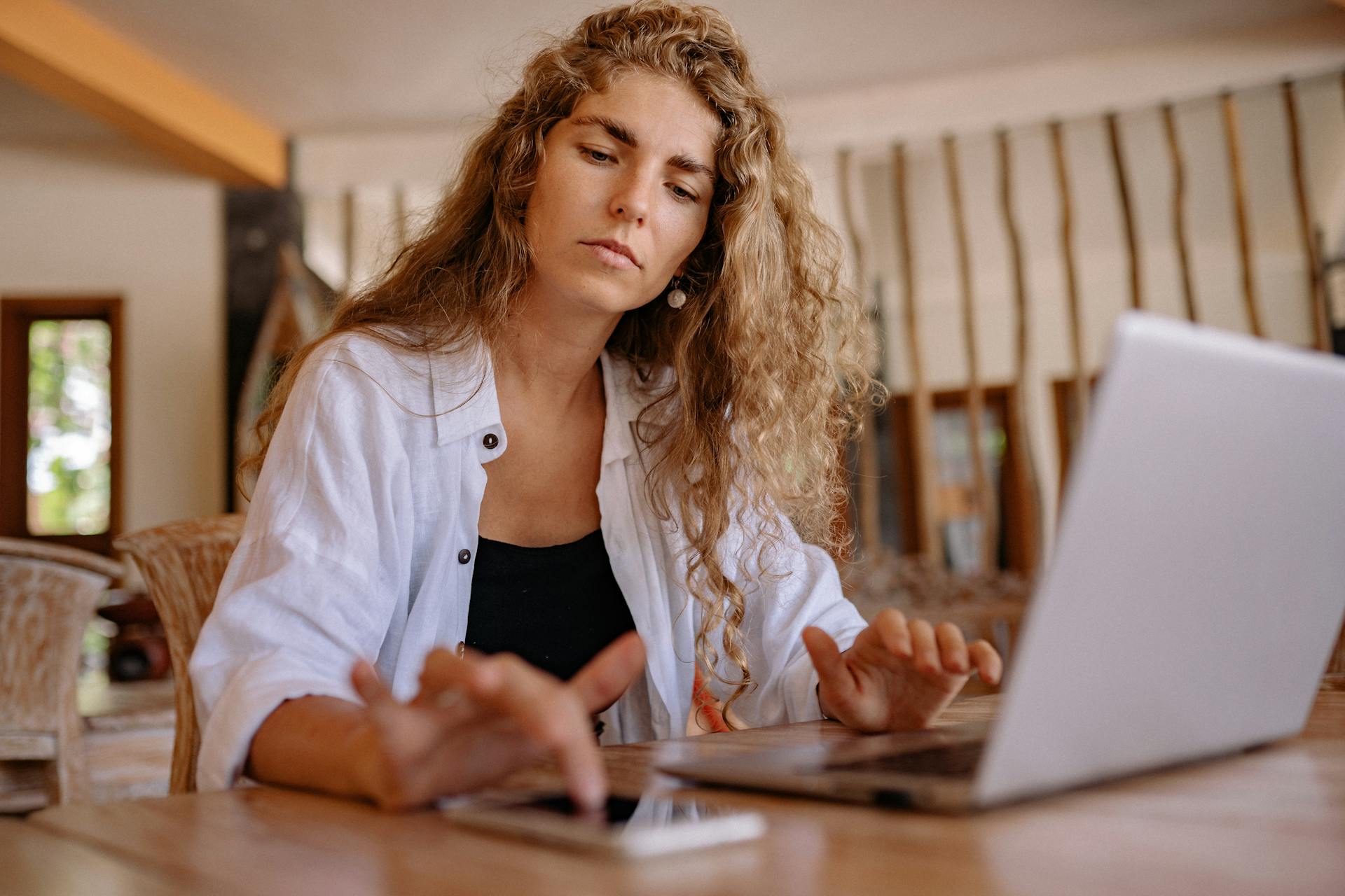 Woman analyzing website above the fold content on a laptop while using a smartphone, focusing on design and user experience.