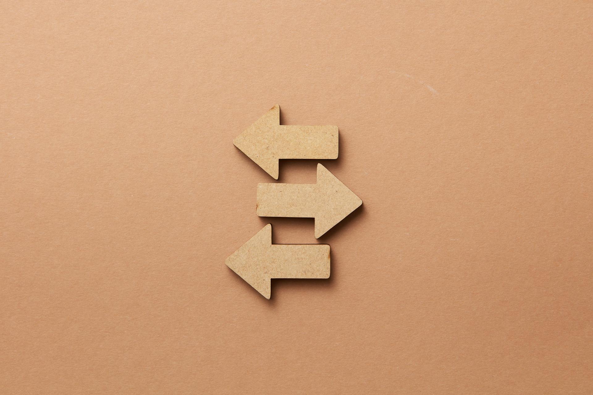 Three wooden arrows pointing in opposite directions on a brown background, representing the differences and overlap between AEO vs GEO strategies.