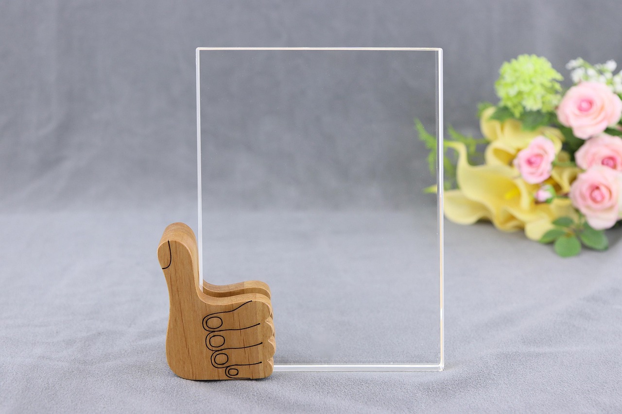 A clear acrylic display stand with a wooden thumbs-up base, set against a gray background with flowers, representing minimalistic product presentation and evolving ecommerce trends 2026 in retail design.