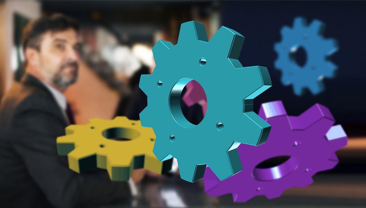 Colorful 3D gears overlaid on a blurred office background, symbolizing automation, backend integration, and operational efficiency in the future of ecommerce and AI-powered business systems.