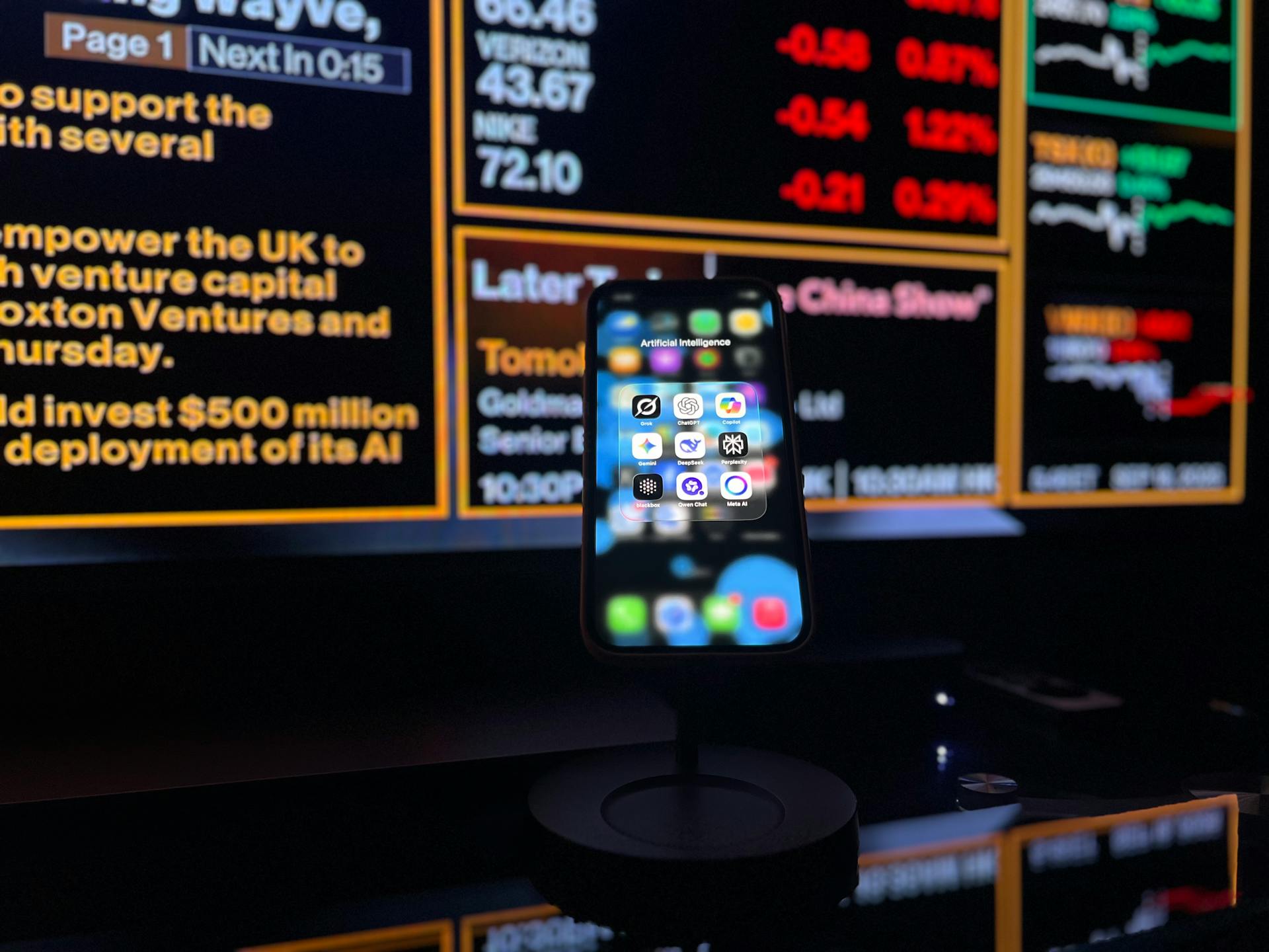 Smartphone displaying a folder of AI apps labeled ‘Artificial Intelligence’, set against a backdrop of financial news screens—illustrating the intersection of AI, AEO and GEO in modern business and search trends.