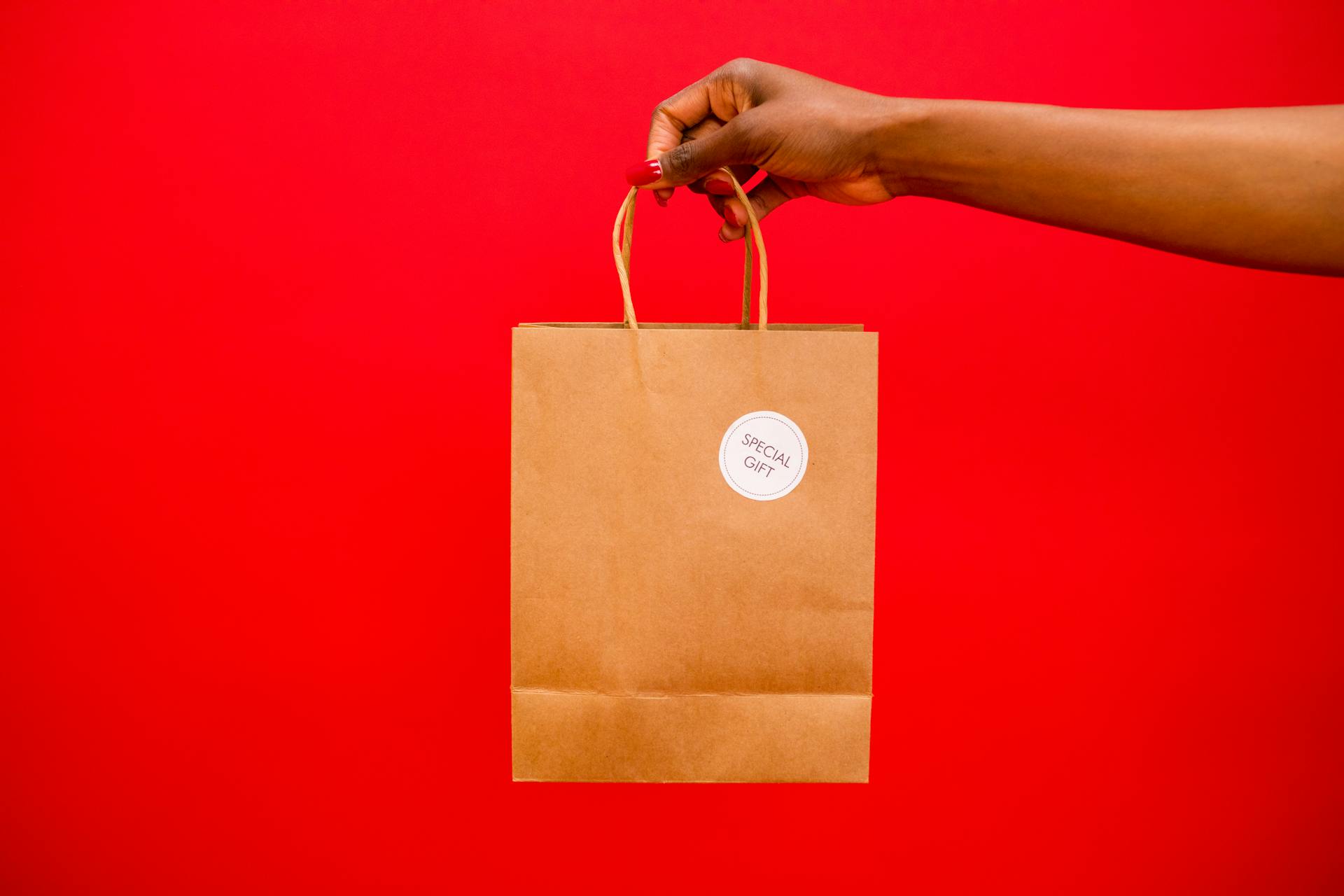 Hand holding shopping bag against red background, symbolizing ecommerce conversion optimization, online sales growth, and successful customer purchase.
