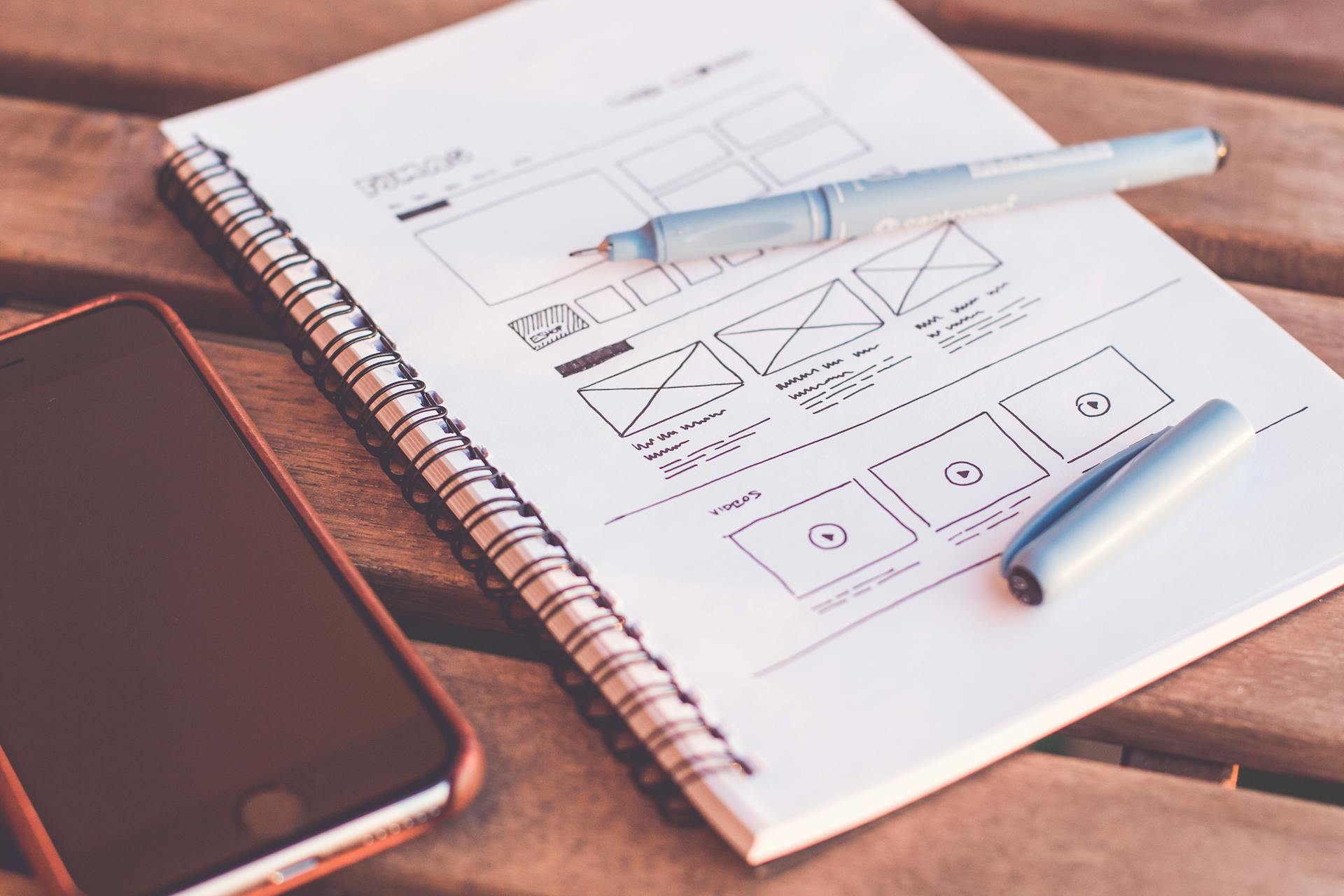 Website wireframe sketch on notebook beside smartphone, illustrating ecommerce conversion optimization, user experience design, and product page layout planning.