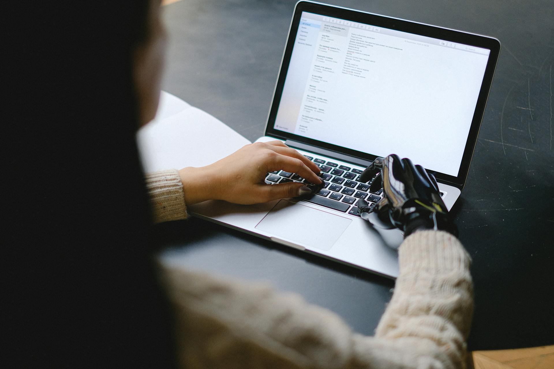 A person with a robotic prosthetic hand typing on a laptop, symbolizing human-AI collaboration and the evolving role of assistive technology and AI in commerce and digital work environments.