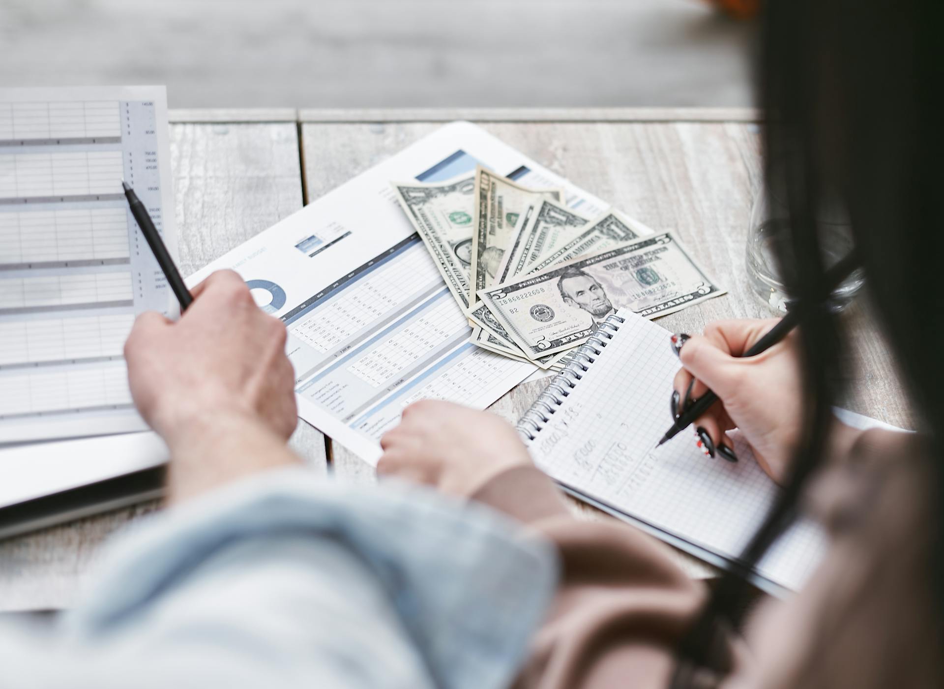 Person reviewing financial reports and writing notes beside cash and charts, representing ecommerce marketing budgeting, campaign ROI analysis, and data-driven ecommerce growth strategy.