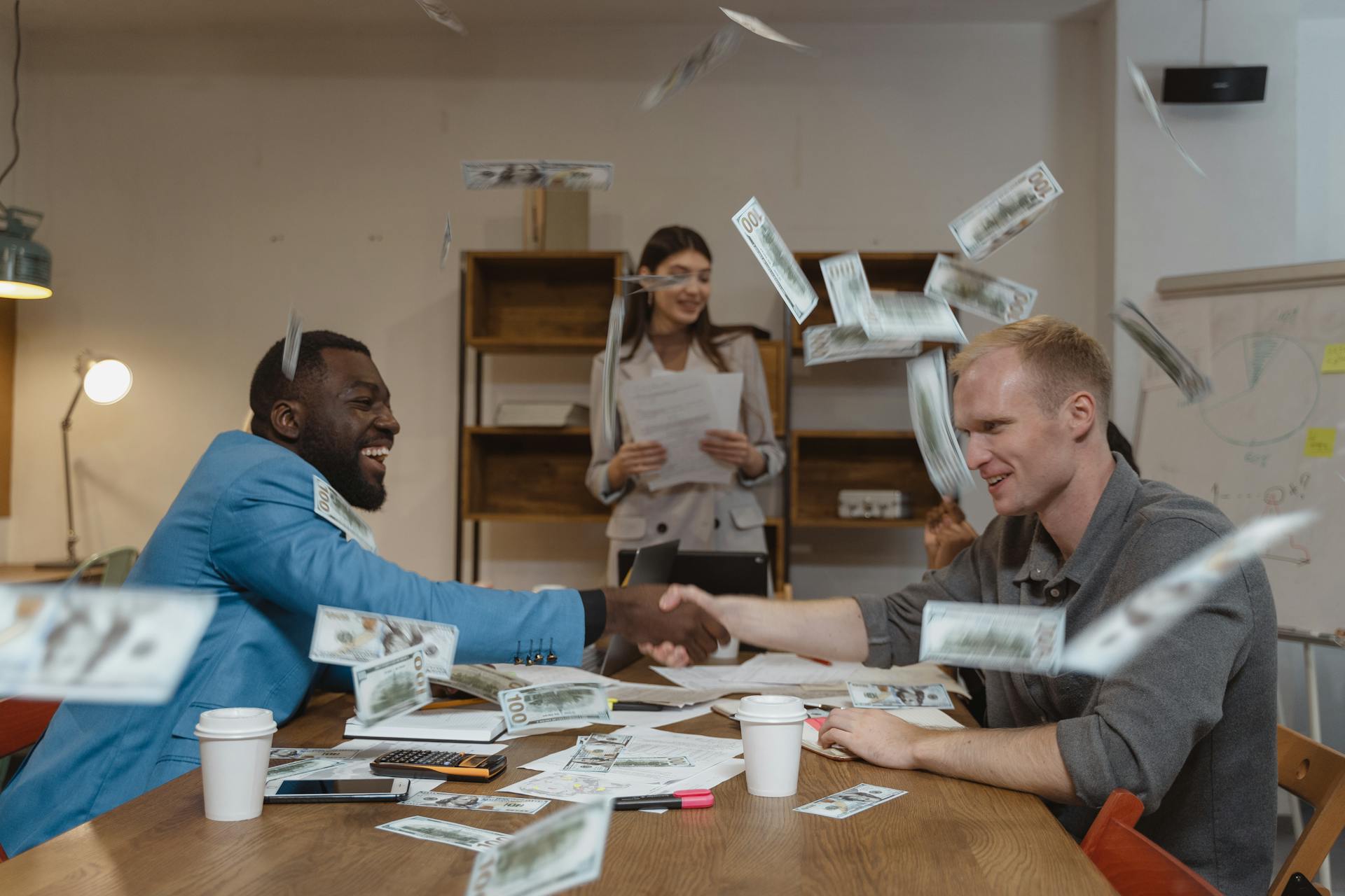 Business team celebrating a successful deal with money flying while shaking hands, representing profitable ecommerce marketing strategies, revenue growth, and successful online business performance.