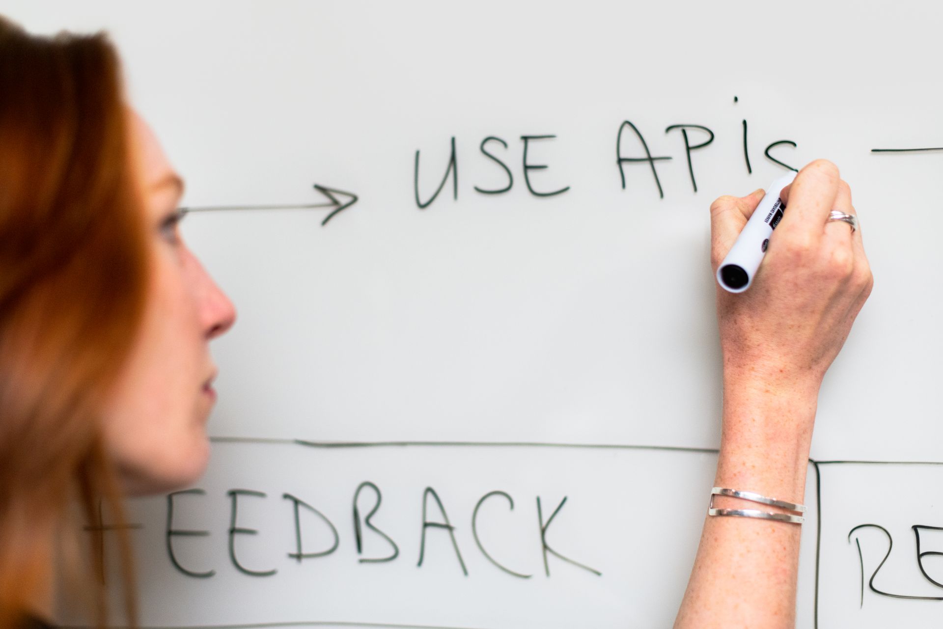 Person writing “Use APIs” on a whiteboard, illustrating backend integrations and API connections used by Shopify apps. Visual representation of how many Shopify apps connect through APIs and how Shopify apps slow down store performance when multiple third-party integrations and frontend scripts accumulate.